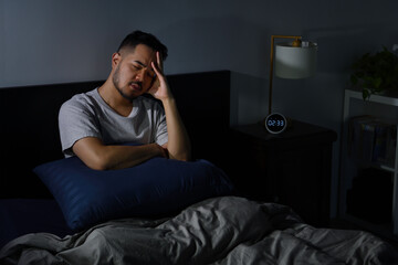 Depressed young Asian man sitting in bed cannot sleep from insomnia