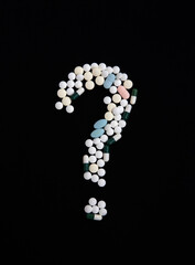 A question mark made of pills on a black background. The concept of vaccination and health protection