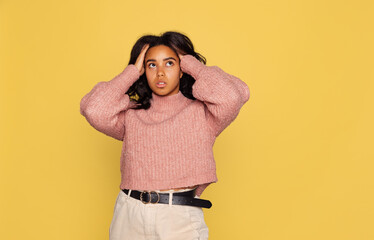 Half-length portrait of young pretty dark skinned girl in warm knitted sweater isolated on yellow background.