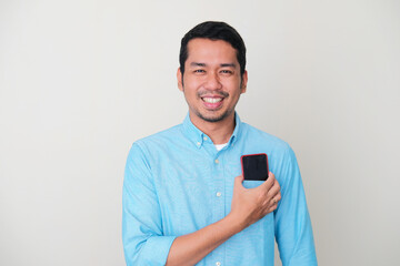 Adult Asian man smiling while putting his mobile phone to his shirt pocket