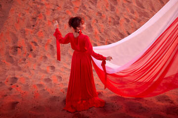 Beautiful young woman or girl with curly hair and in red dress with a light flying fabric on the...