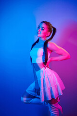 In skirt. Fashionable young woman standing in the studio with neon light