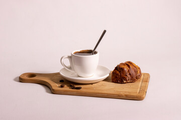 Cup with brewed coffee and eclair on wooden board