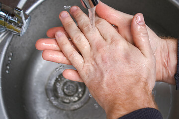 A man washes his hands with soap in the kitchen sink after washing potatoes.