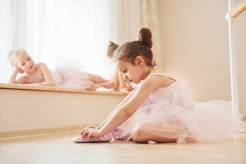 Girl sits on the floor. Little ballerinas preparing for performance by practicing dance moves