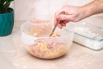 A man mixes minced meat, cabbage, onions, carrots, rice, spices in a bowl for lazy cabbage rolls on the table.