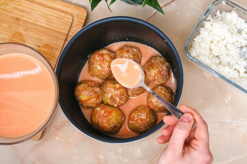 A man puts lazy cabbage rolls into a multicooker bowl and pours tomato and sour cream sauce over them.