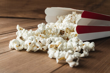 Popcorn spilled from a paper striped box. Traditional cardboard bucket with kernels. Cinema film or movie theater composition with copy space on wooden background.