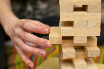 close up, the hand of a man, a girl, pulls a piece of wooden bar from the tower structure of a toy house during a board game