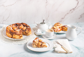 Portion of homemade cinnamon rolls on a white plate on a white table with coffee and pastry buns for breakfast. Traditional Swedish and Danish recipe.