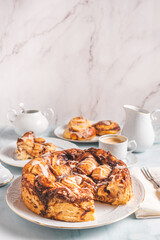 Homemade cinnamon rolls on a white plate on a white table with coffee and pastry buns for breakfast. Traditional Swedish and Danish recipe.