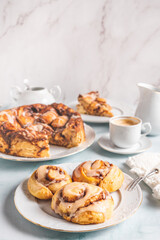 Homemade cinnamon rolls on a white plate on a white table with coffee and pastry buns for breakfast. Traditional Swedish and Danish recipe.