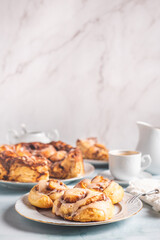 Homemade cinnamon rolls on a white plate on a white table with coffee and pastry buns for breakfast. Traditional Swedish and Danish recipe.