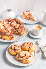 Homemade cinnamon rolls on a white plate on a white table with coffee and pastry buns for breakfast. Traditional Swedish and Danish recipe.