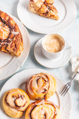 Homemade cinnamon rolls on a white plate on a white table with coffee and pastry buns for breakfast. Traditional Swedish and Danish recipe.