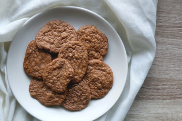 Plate of healthy, gluten free and high protein cookies, made with bananas, eggs, chia seeds and almonds. White tablecloth and wooden background. Flat lay.