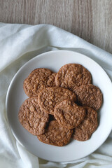 Plate of healthy, gluten free and high protein cookies, made with bananas, eggs, chia seeds and almonds. White tablecloth and wooden background. Flat lay.