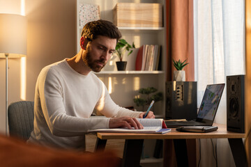 Serious concentrated bearded guy is laboring with pleasure at the laptop while writing something