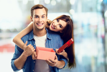 Consumer credit, celebrating, sales, rebates concept - happy amased couple opening gift box. Man and woman standing over blurred modern interior or mall background.