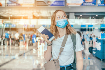 COVID-19 Happy blonde hair female tourist with a backpack in a protective medical mask with a passport while waiting for the passport check of the tourist at the airport
