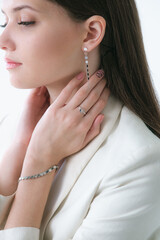Trending silver jewelry set on a beautiful young girl in a white fashionable jacket  with long dark hair. Beauty and fashion 
