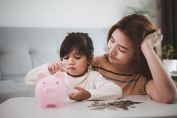 Mother and daughter putting coins into piggy bank. Family budget and savings concept. Junior Savings Account concept