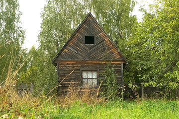 Small abandoned wooden house in the village among the greenery in summer. House on a suburban plot for a summer vacation in a third world country. A crumbling house in the countryside.