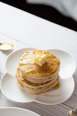 Pancake with butter and honey maple syrup set on white cafe table.