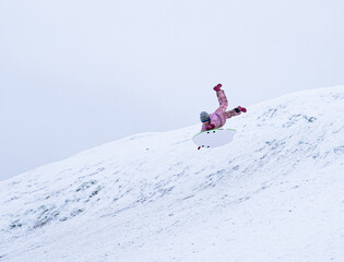 Naklejka na ściany i meble A child very quickly slides down a snow-covered mountain on a sled. Winter walk