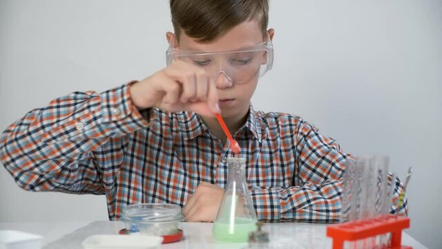 Teen boy is wearing protective glasses and doing chemistry experiments with gas reaction. He is mixing soda, citric acid and green liquid in flask. Online education, homeschooling and science concept.