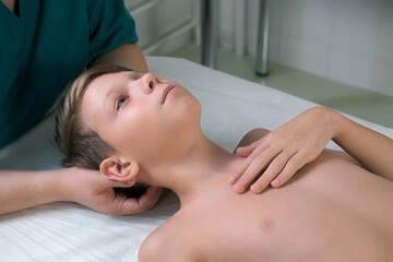 Obraz na płótnie Canvas Session of craniosacral therapy, cure of teen boy's back of the head and neck by a doctor therapist. Craniosacral therapist touches boy's head and corrects spine at hospital. Boy is lying on couch.