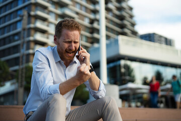 Businessman talking to the phone while sitting on the stairs. Angry upset man talking to the phone.