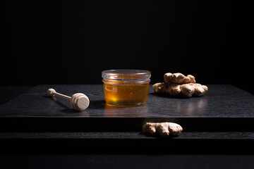 Miel de abeja en un frasco de vidrio con jengibre y un gotero de madera sobre fondo negro. Aislado