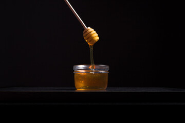 Verter miel de abeja con un gotero de madera en un frasco de vidrio sobre fondo negro. Aislado
