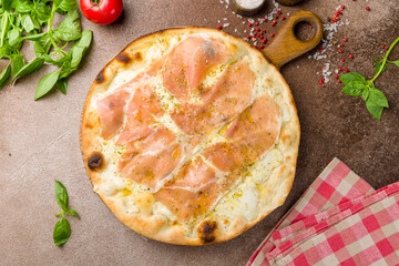 Pizza with prosciutto, cheese and oregano on wooden board top view on brown concrete table