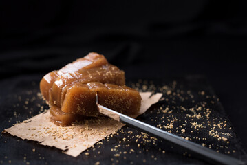 Dulce pasta de gelatina de membrillo dorado con sésamo molido y un tenedor sobre una placa de madera negra
