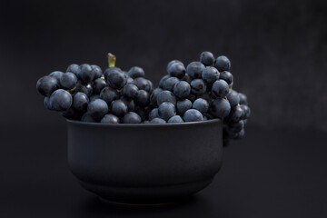 Uvas azules dentro de un recipiente negro sobre fondo negro