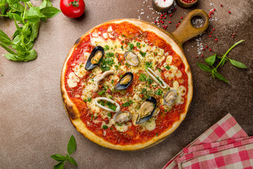 Pizza with seafood, cheese and tomato sauce on wooden board top view on brown concrete table