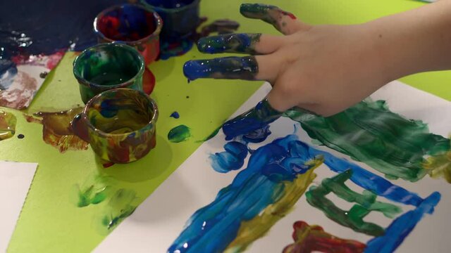 Child draws with finger paints in kindergarten or home, close up. Concept of child development.