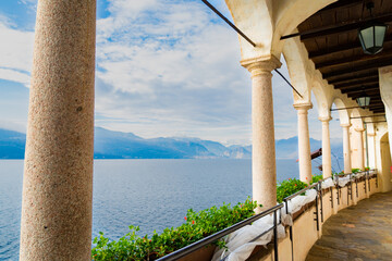 Columns and arcade in the famous "Eremo di Santa Caterina del Sasso" (meaning: "Saint Catherine of the stone hermitage"). Blue waters of Lake Maggiore on the background, Italy.