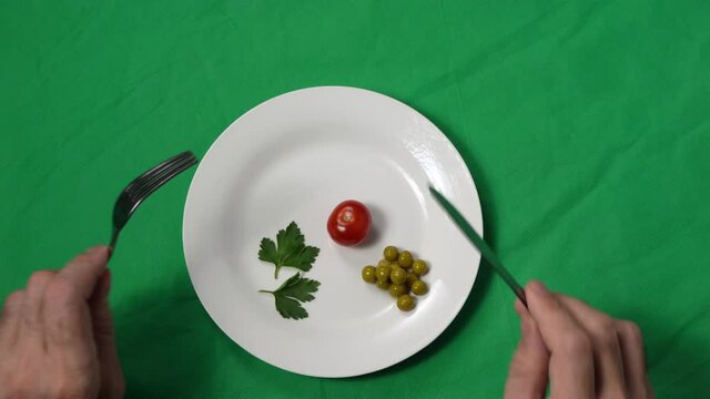 A man's hands move closer to the plate of meager food. Portion control. The concept of weight loss and healthy eating. Natural ingredients. Vegetables and healthy eating. Top view