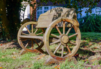 Fototapeta na wymiar old wooden wagon made into a quirky garden seat. Crafted outdoor bench made from an old cart with wooden spoked wheels. 