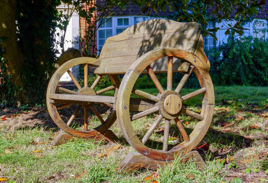 old wooden wagon made into a quirky garden seat. Crafted outdoor bench made from an old cart with wooden spoked wheels. 