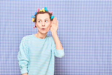 Woman with hair curlers is placing hand near ear and eavesdropping