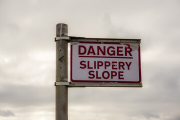 signpost with warning sign reading Danger slippery slope. Rusty sign post on coastal slipway. 