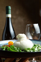 Burata cheese in a plate. Against the background of a bottle of wine and glasses.