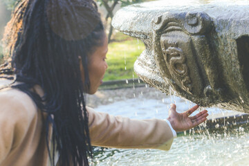 african woman touching pure water from an old public fountain