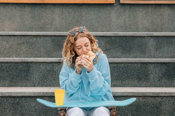 Young woman bite street food outdoors and drinking coffee.