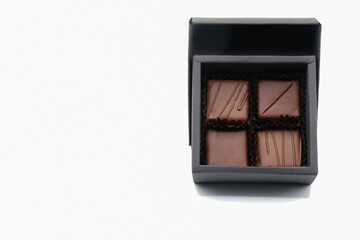 Four pralines in a square black box on the white background. Small chocolate gift set. Copy space. 