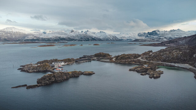 Cozy village of Hamn surrounded by the clear icy sea in Andsfjord, Senja and northern Norway under dramatic skies. Scandinavian autumn. Snow-covered hills in the background